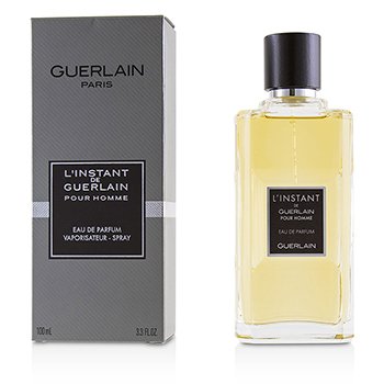 Clear glass bottle with a black cap, containing a pale yellow fragrance, alongside a sleek gray box featuring the brand name "Guerlain" and product details in white text.