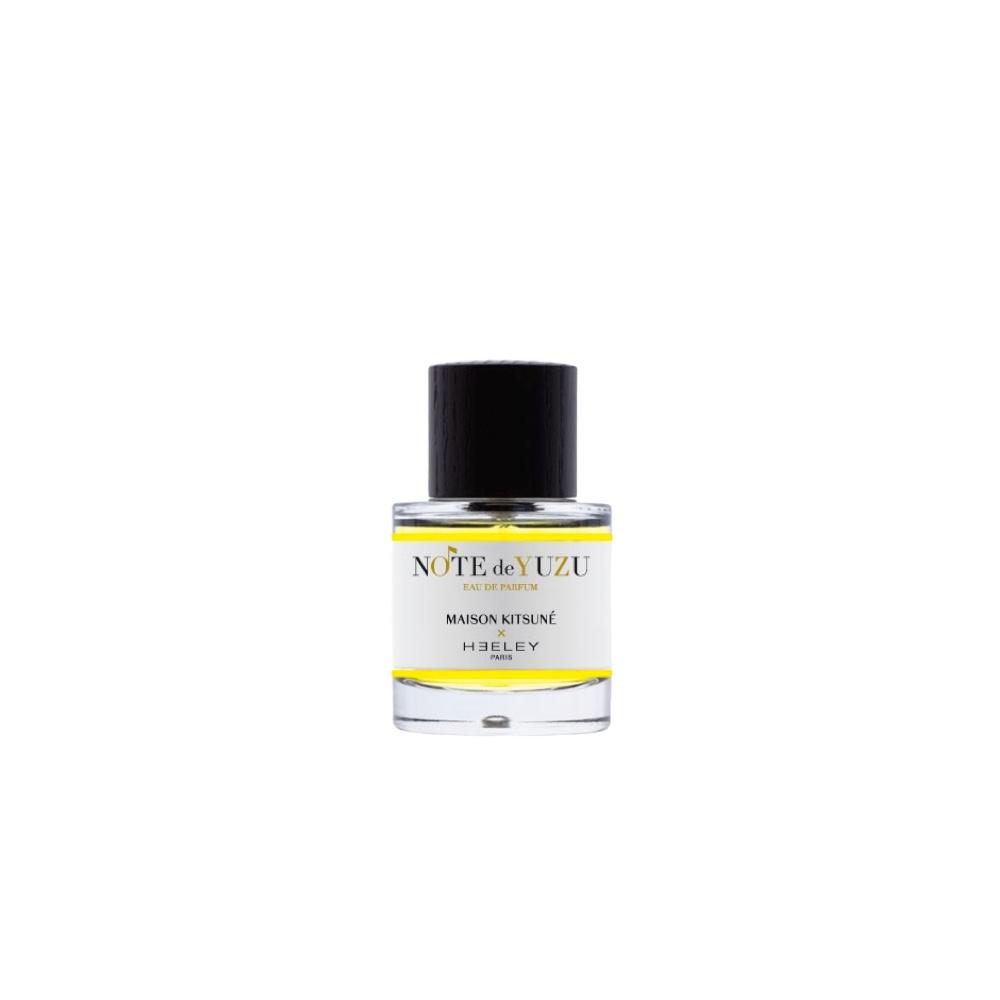Clear glass bottle with a black cap, containing a bright yellow liquid labeled "NOTE DE YUZU" and "MAISON KITSUNE X HEELEY," showcasing a minimalist design.