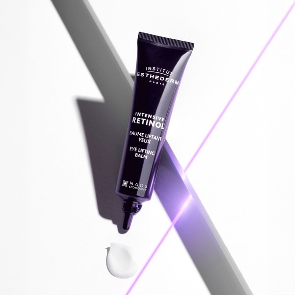 Dark purple tube of Institut Esthederm Intensive Retinol Eye Lifting Balm with a pointed nozzle, featuring white text and a small droplet of balm on a white surface.
