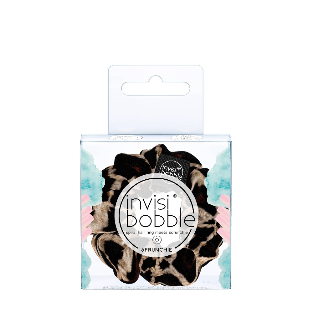 A black and brown leopard print scrunchie made of soft fabric, packaged in a clear box with a colorful design and the Invisibobble logo prominently displayed.