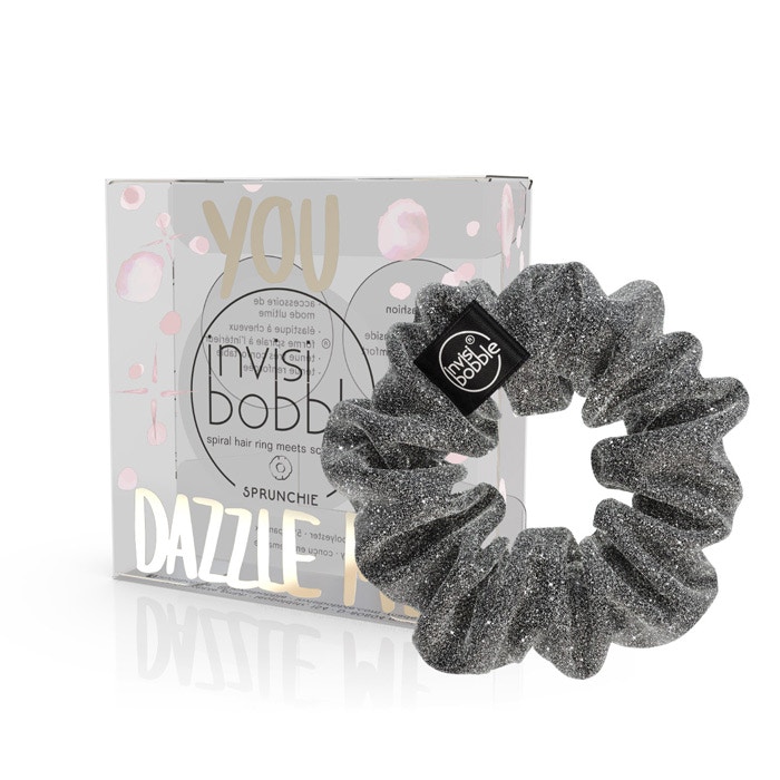 Black glittery scrunchie hair tie with a spiral design, featuring a small black logo tag, displayed in a silver box with pink and gold accents labeled "You Dazzle Me."