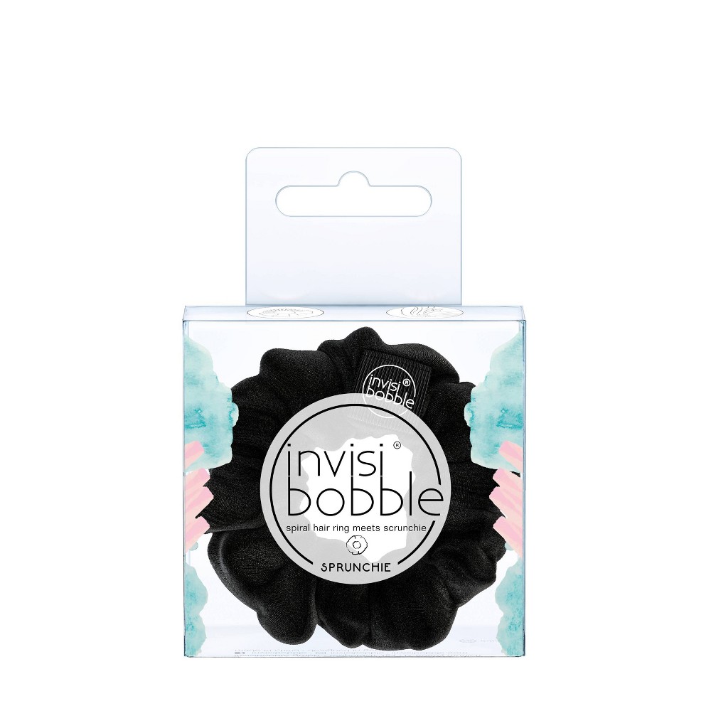 A black scrunchie made from soft fabric, featuring a spiral hair ring design, packaged in a clear box with pastel watercolor accents and the Invisibobble logo.