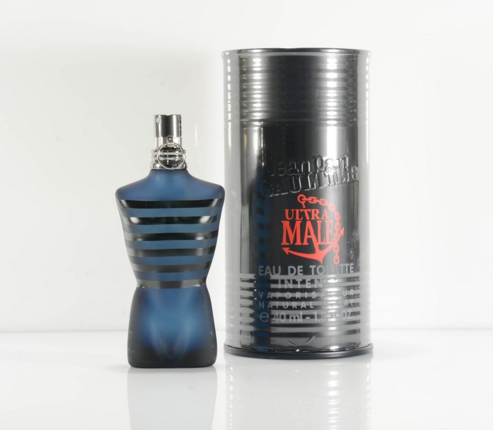 Dark blue glass bottle shaped like a torso, featuring black stripes, with a silver cap, alongside a cylindrical black and silver box labeled "Ultra Male Eau De Toilette 40ml."