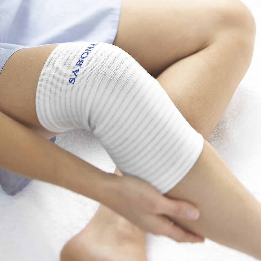 White knee support featuring ribbed texture and "SABONA" branding, designed for comfort and relief, with copper-infused material for added therapeutic benefits.