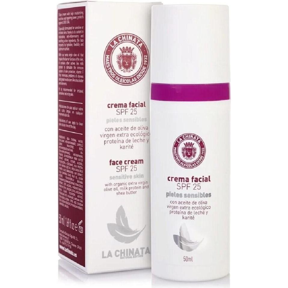 White cylindrical bottle with a pink band, labeled "Crema Facial SPF 25" for sensitive skin, featuring olive oil and shea butter, alongside a red and white box design.