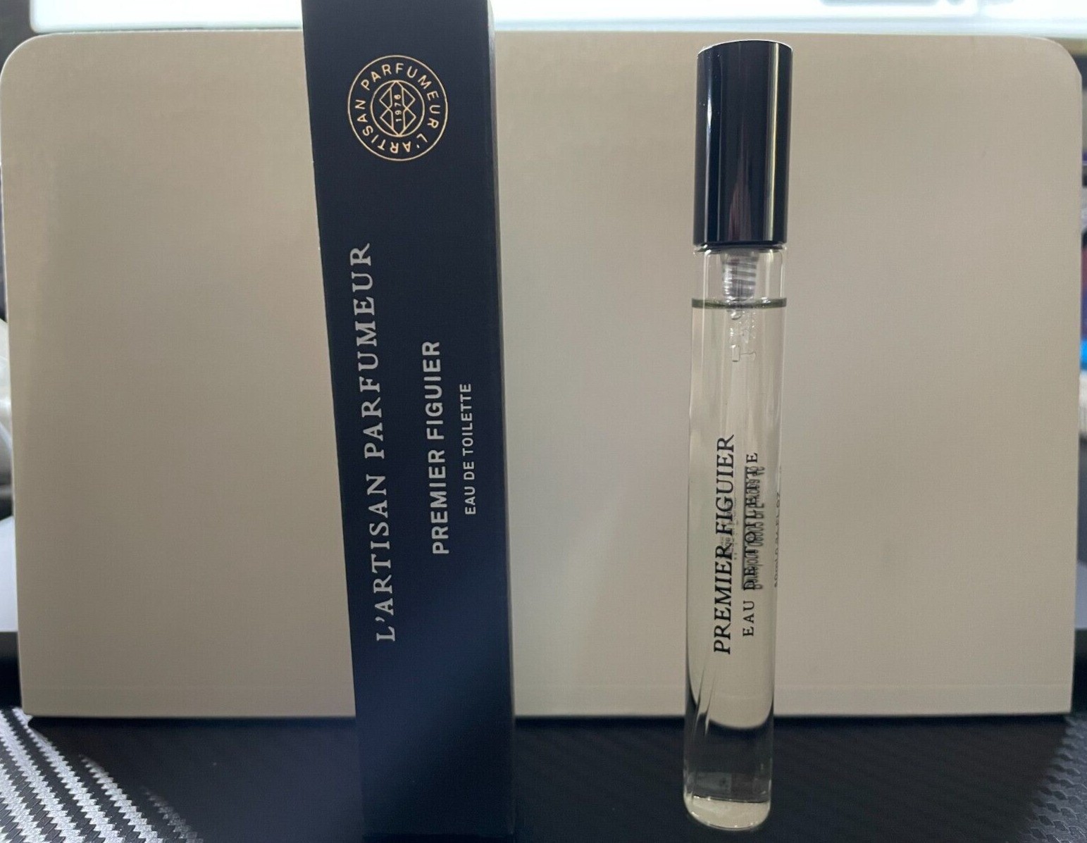 L'Artisan Premier Figuier Eau De Toilette 10ml spray in a clear glass bottle with a black cap, alongside a navy blue box featuring gold lettering.