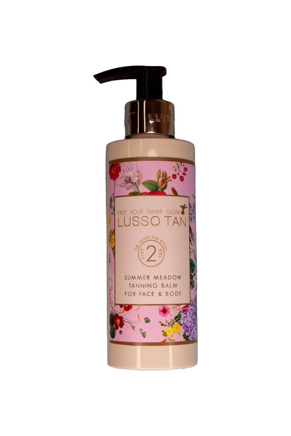 Lusso Tan Summer Meadow Tanning Balm in a pink bottle adorned with colorful floral designs, featuring a pump dispenser and a label indicating it's for face and body.