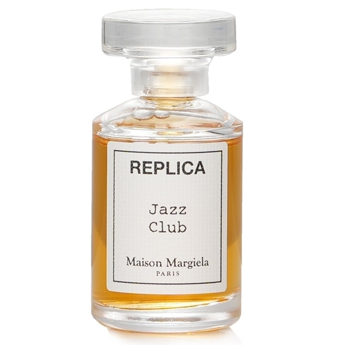 Clear glass mini perfume bottle with a round stopper, featuring a label that reads "REPLICA Jazz Club" and "Maison Margiela Paris," filled with amber-colored liquid.