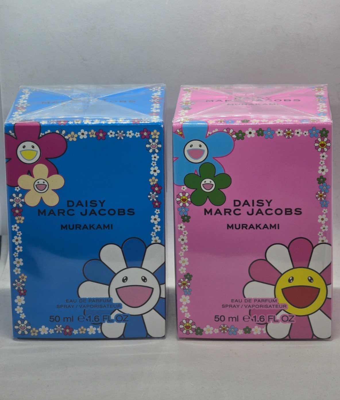 Brightly colored packaging for Marc Jacobs Daisy Murakami Eau De Parfum, featuring a pink box with a smiling flower design and a blue box, both labeled 50ml.