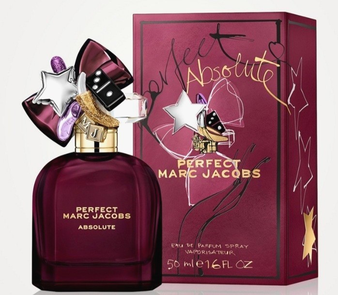 Deep purple glass bottle with a star-shaped cap, adorned with colorful charms, beside a matching burgundy box featuring gold and white text, labeled "Perfect Absolute."