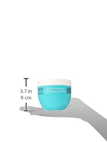 A turquoise jar of Moroccanoil Weightless Hydrating Mask held in a hand, featuring a white lid and text detailing its hydrating properties.
