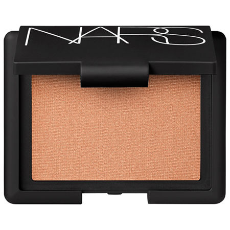 Nars Blush Illicit features a soft peachy-pink powder with a subtle shimmer, housed in a sleek black compact with the Nars logo prominently displayed on the lid.