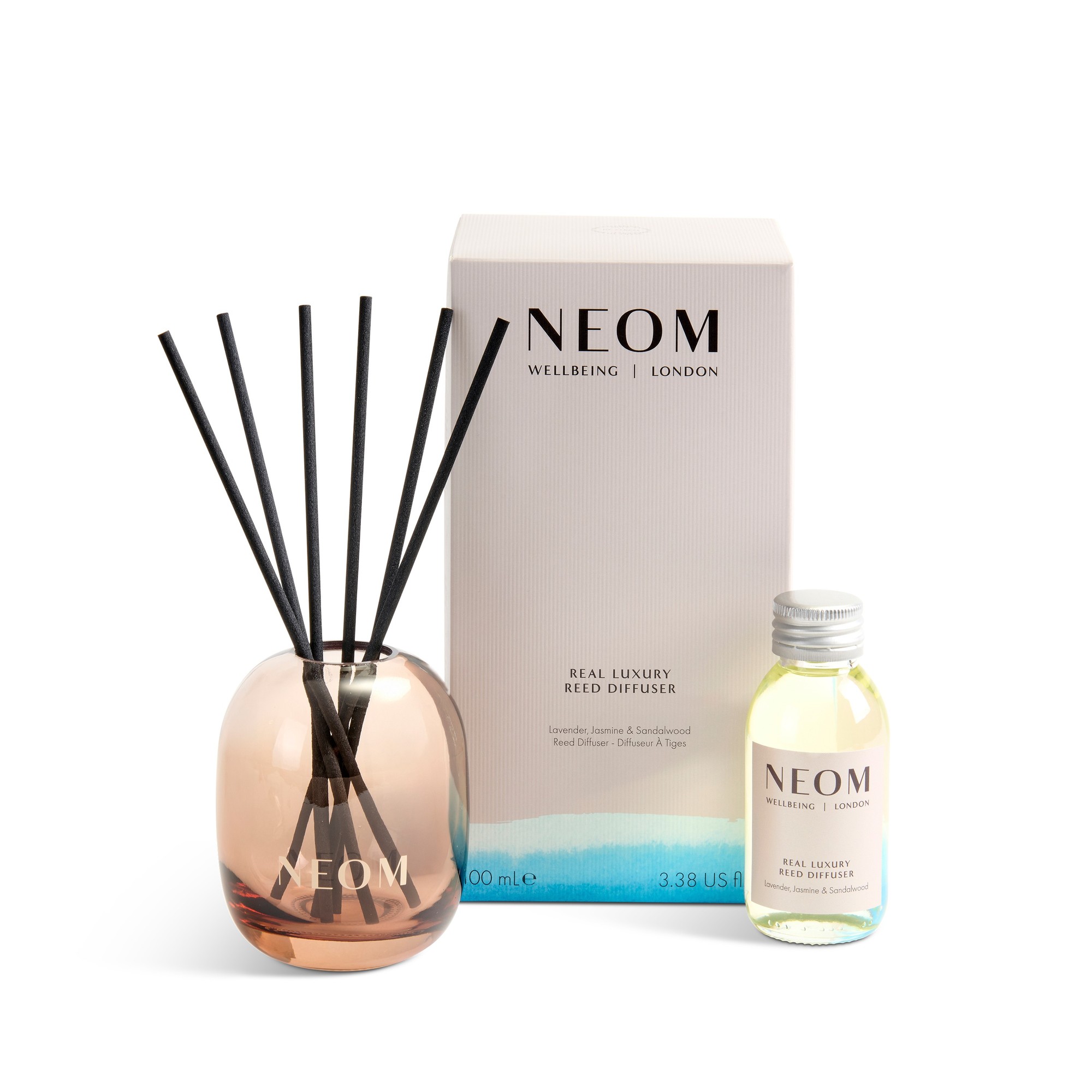 NEOM Real Luxury Reed Diffuser Refill in a clear glass bottle, accompanied by a sleek, rose gold diffuser with black reeds, packaged in a stylish box with a soft gradient design.