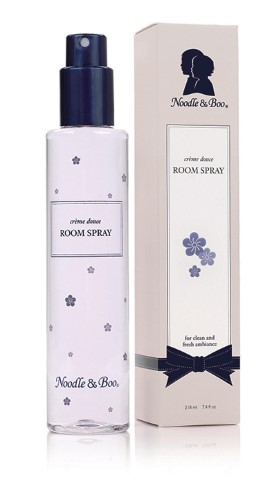 Clear glass bottle with a navy blue spray nozzle, labeled "Room Spray" with floral accents; packaged in a cream-colored box featuring a silhouette and blue flower design.