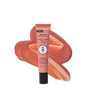 Nudestix Nudescreen Blush Tint SPF 30 in a soft peach tube, featuring a matte finish and a swatch of creamy blush in a warm coral shade behind it.