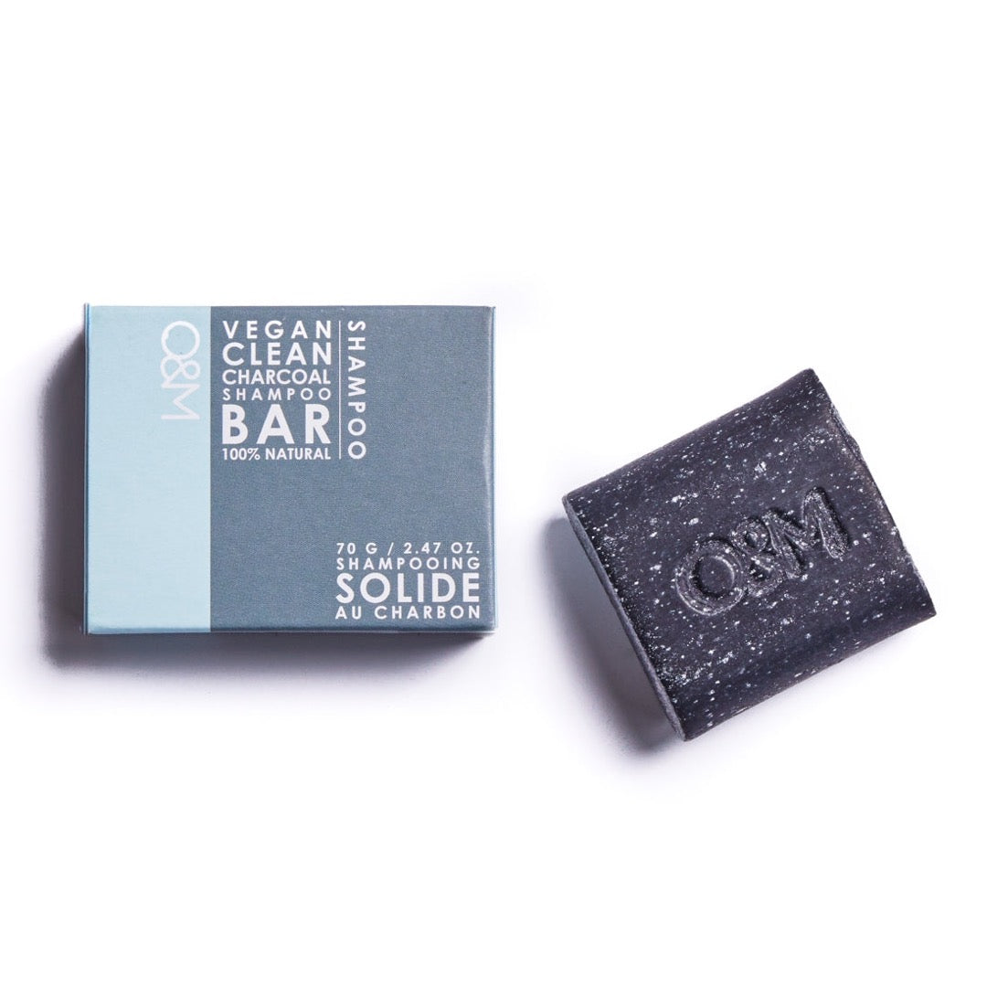 A rectangular box in light blue and gray packaging labeled "O & M Charcoal Shampoo Bar" next to a black, textured shampoo bar with the letters "O&M" embossed on it.