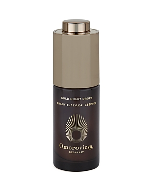 Dark glass bottle with a gold metallic cap, featuring a sunburst logo and "Omorovicza Gold Night Drops" text, designed for nighttime skincare.
