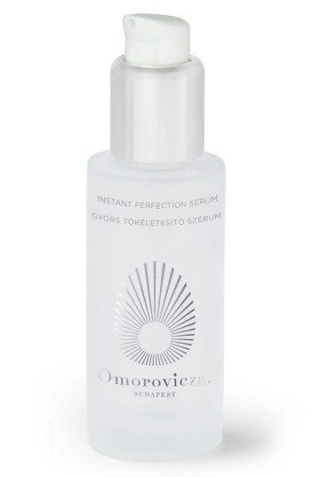 Clear glass bottle with a frosted finish, featuring a white pump dispenser, labeled "Omorovicza Instant Perfection Serum" with a sunburst design and silver text.