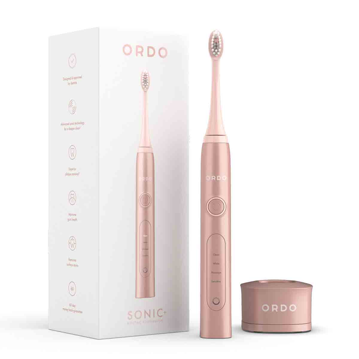Sleek rose gold ORDO Sonic+ electric toothbrush with a travel cap, featuring a textured brush head, control buttons, and a matching cylindrical base, displayed alongside its packaging.