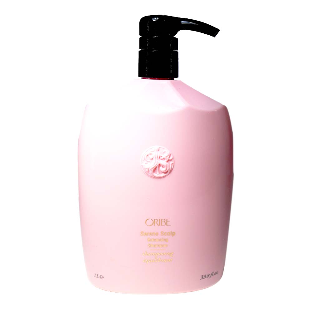 Light pink, ergonomic bottle of Oribe Serene Scalp Balancing Shampoo with a black pump, featuring a decorative emblem and labeled with product details in gold text.