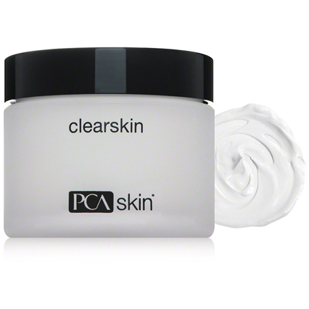 Clear, frosted jar with a black lid labeled "clearskin" and "PCA skin," accompanied by a swirl of white cream beside it.