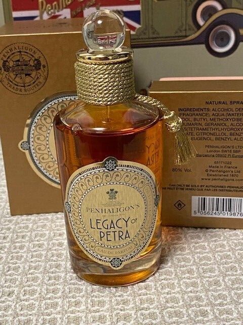 Legacy of Petra Eau De Parfum by Penhaligon's features a clear glass bottle with a gold cap, adorned with a decorative label and a tassel, set against a patterned box.