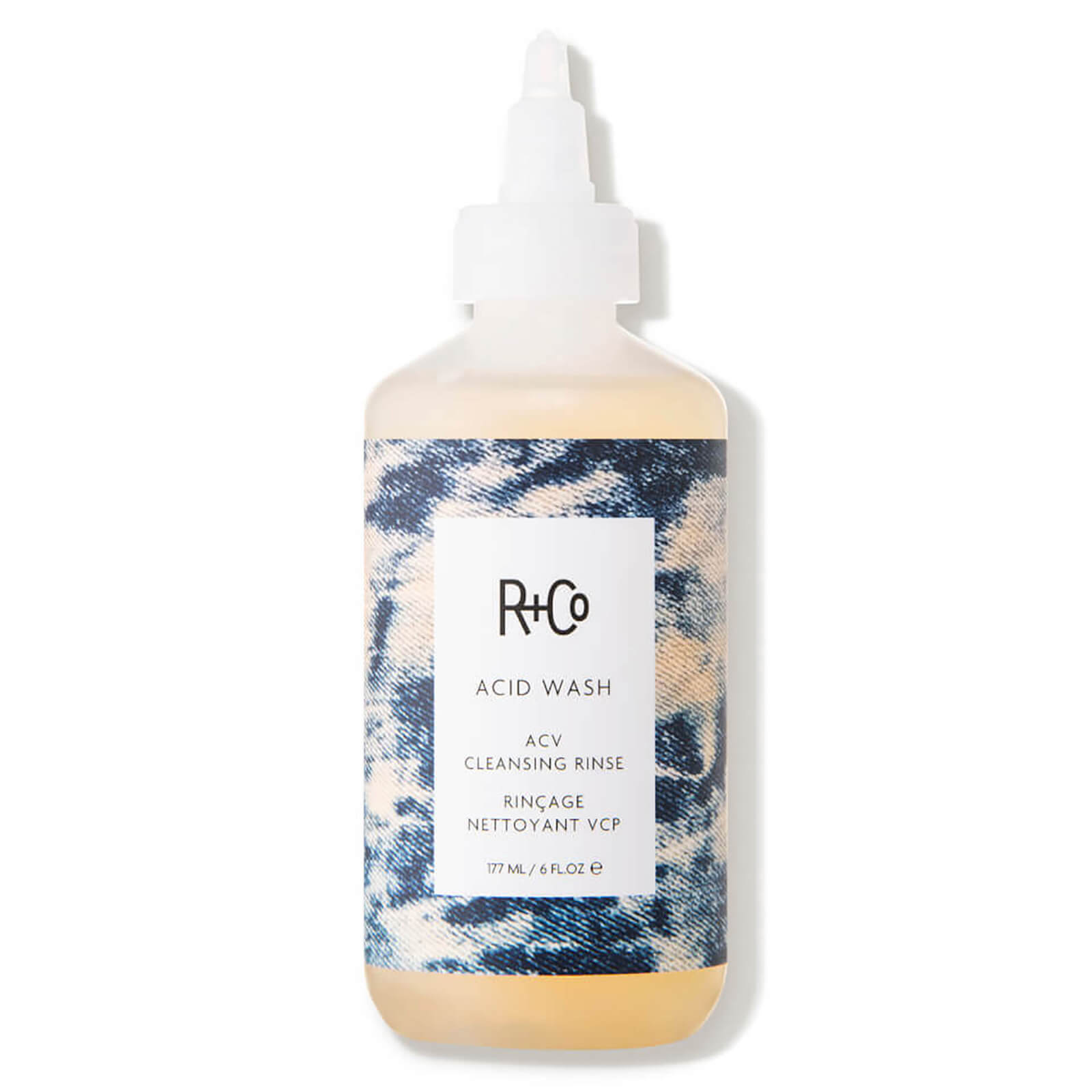Clear bottle with a white label featuring "R+Co" logo, surrounded by a blue and white tie-dye pattern, containing a light amber liquid, labeled as "LOST TREASURE APPLE CIDER VINEGAR CLEANSING RINSE."