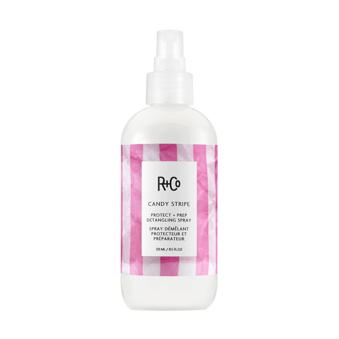 Clear spray bottle with a white pump top, featuring a pink and white striped label that reads "R+Co CANDY STRIPE Detangling Spray" in bold black text.