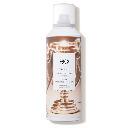 R+Co Trophy Shine + Texture Spray in a 198ml silver and white canister featuring a trophy design, rich in vitamins and suitable for all hair types.