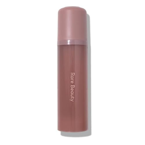 A sleek, cylindrical bottle of Rare Beauty's Find Comfort Body & Hair Fragrance Mist in a soft mauve color, featuring a pink cap and the brand name elegantly printed in white.