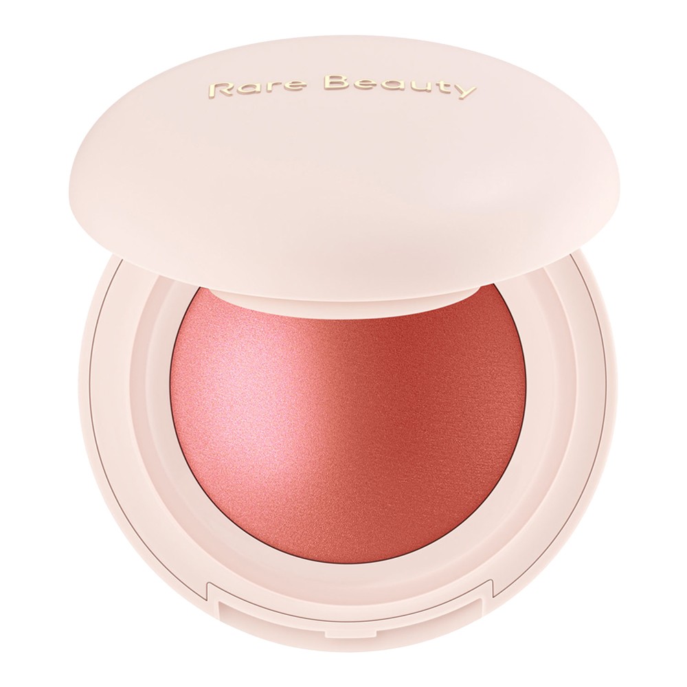 Soft pink compact with a smooth, rounded lid, featuring "Rare Beauty" embossed on top, containing a luminous coral blush inside.