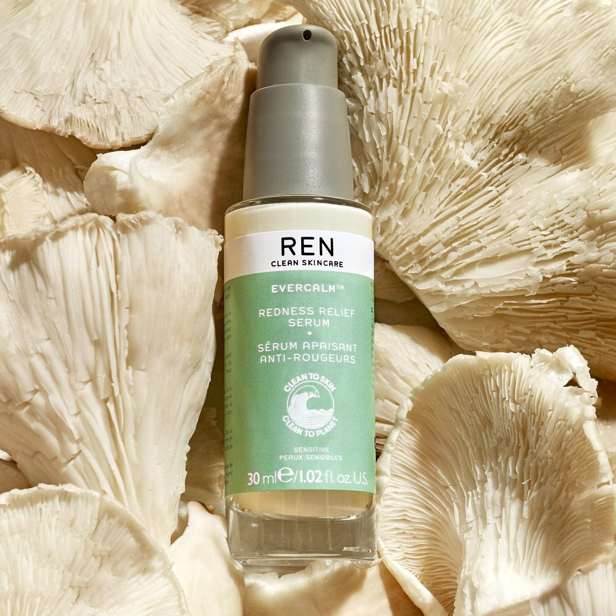 Light green glass bottle with a pump top, labeled "REN Evercalm Redness Relief Serum," surrounded by textured white mushroom-like material.