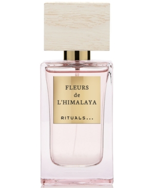 Clear glass perfume bottle with a light pink liquid, featuring a wooden cap and a gold label reading "Fleurs de L'Himalaya" by Rituals.