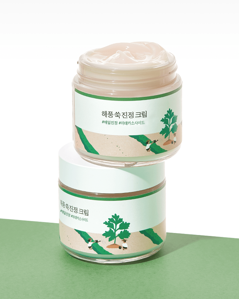 Two jars of Round Lab Mugwort Calming Cream, featuring a pastel green label with illustrations of mugwort leaves and a calming design, showcasing a creamy texture.