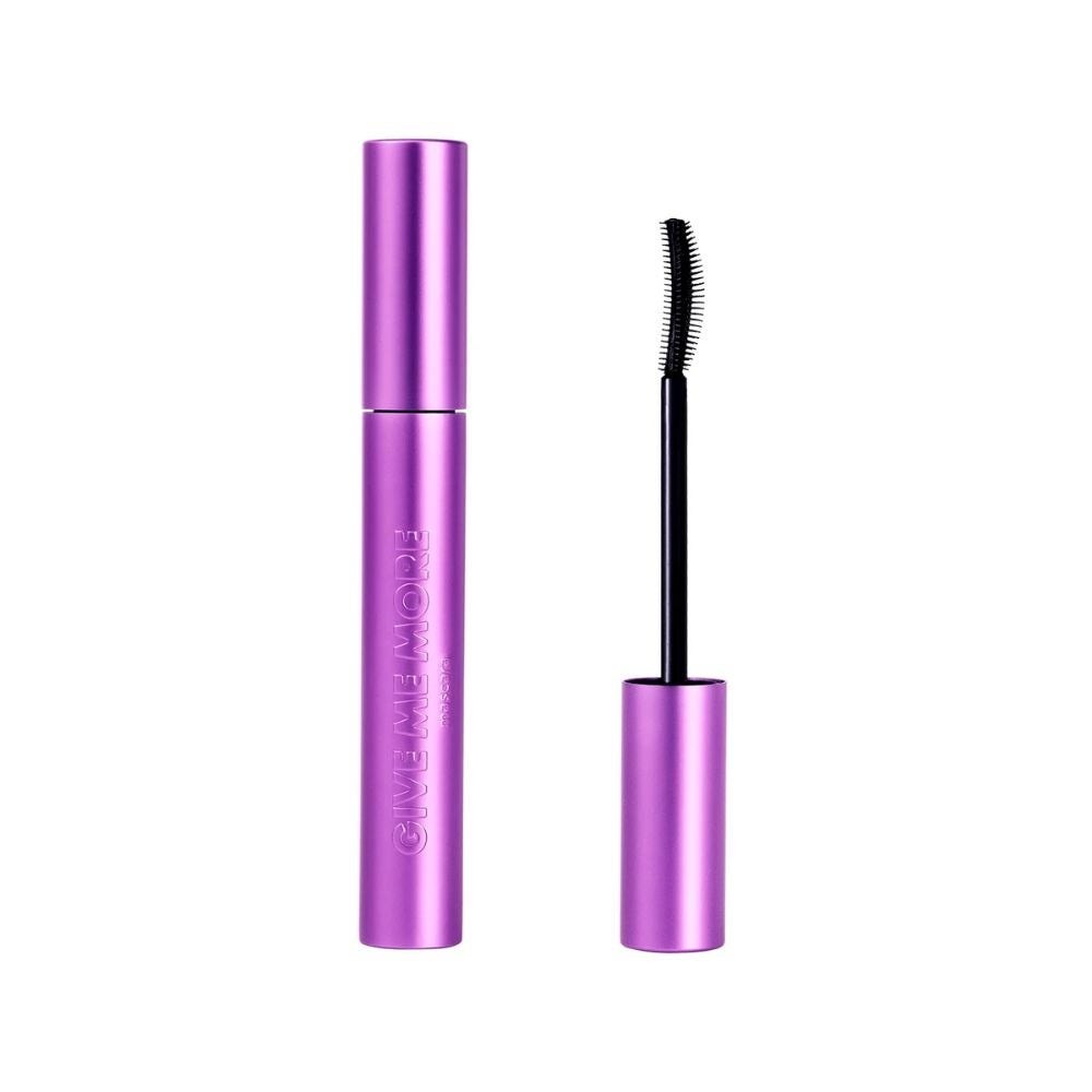 Purple metallic mascara tube labeled "GIVE ME MORE" with a black, curved brush applicator beside it, showcasing its sleek design and unique bristle shape.