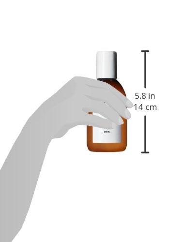 Amber bottle of Sachajuan Normal Hair Shampoo, 8.4 oz, held by a hand, with a white cap and minimalist label, measuring 5.8 inches tall.