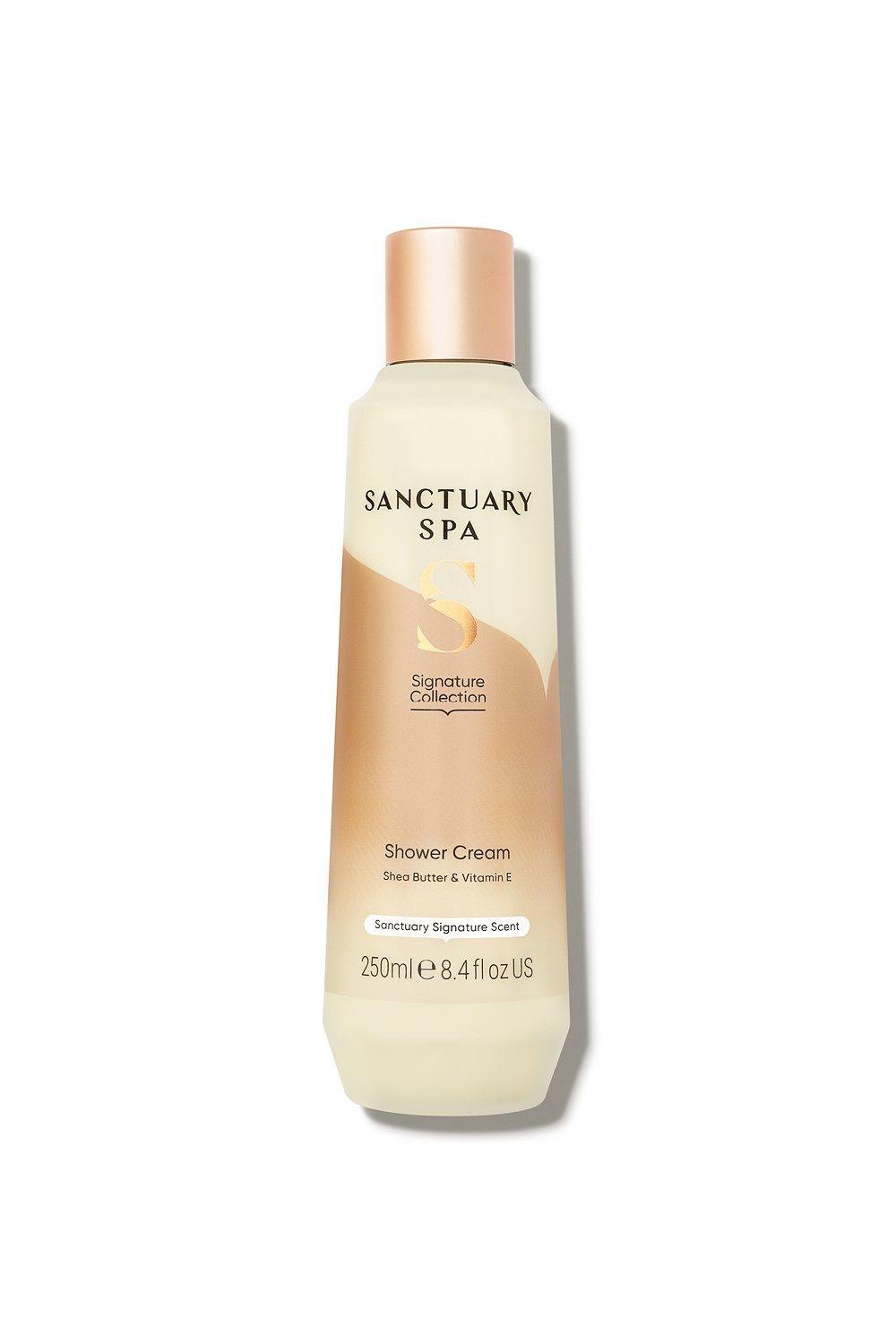 Creamy white bottle with a gold and peach label, featuring "Sanctuary Spa" and "Signature Collection," containing 250 ml of soothing shower cream enriched with shea butter and vitamin E.