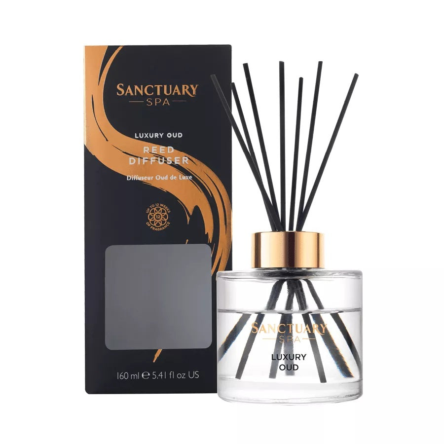 Clear glass diffuser bottle with a gold lid, featuring black reed sticks, accompanied by a sleek black and gold box labeled "Sanctuary Spa Luxury Oud," 160ml.