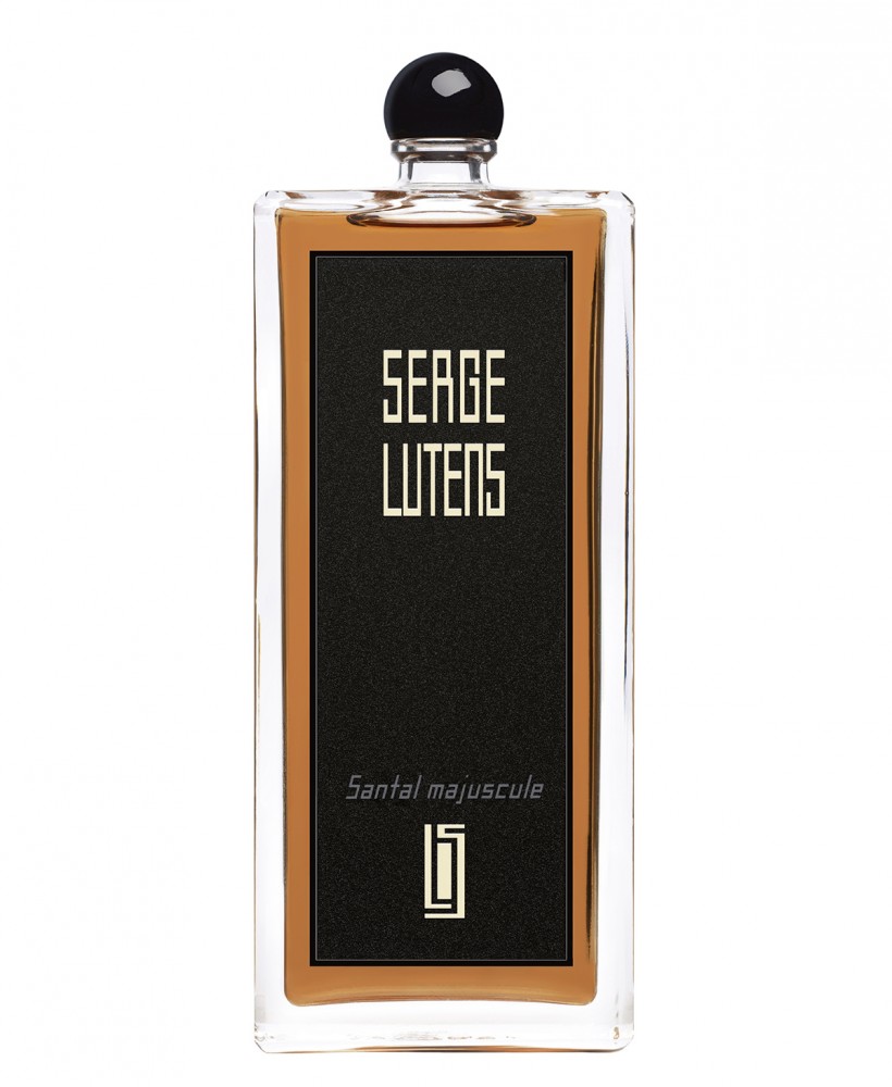 Clear glass bottle with a black rectangular label featuring gold text, containing amber-colored perfume, topped with a round black cap.