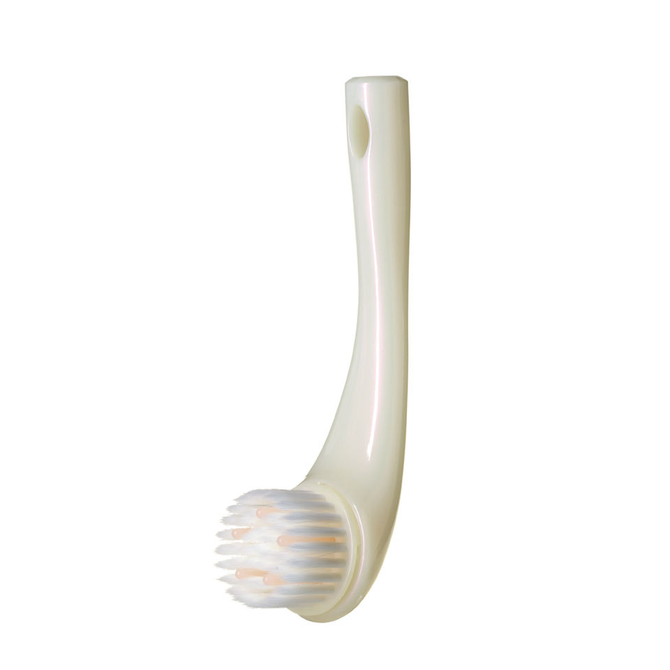Cream-colored cleansing massage brush with a curved handle and soft white bristles, designed for facial cleansing and massage.