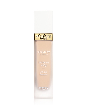 Transparent glass bottle with a gold and white cap, featuring the label "Sisley Paris Sisleya Le Teint Anti-Aging Foundation" in elegant black font, showcasing a light beige foundation inside.