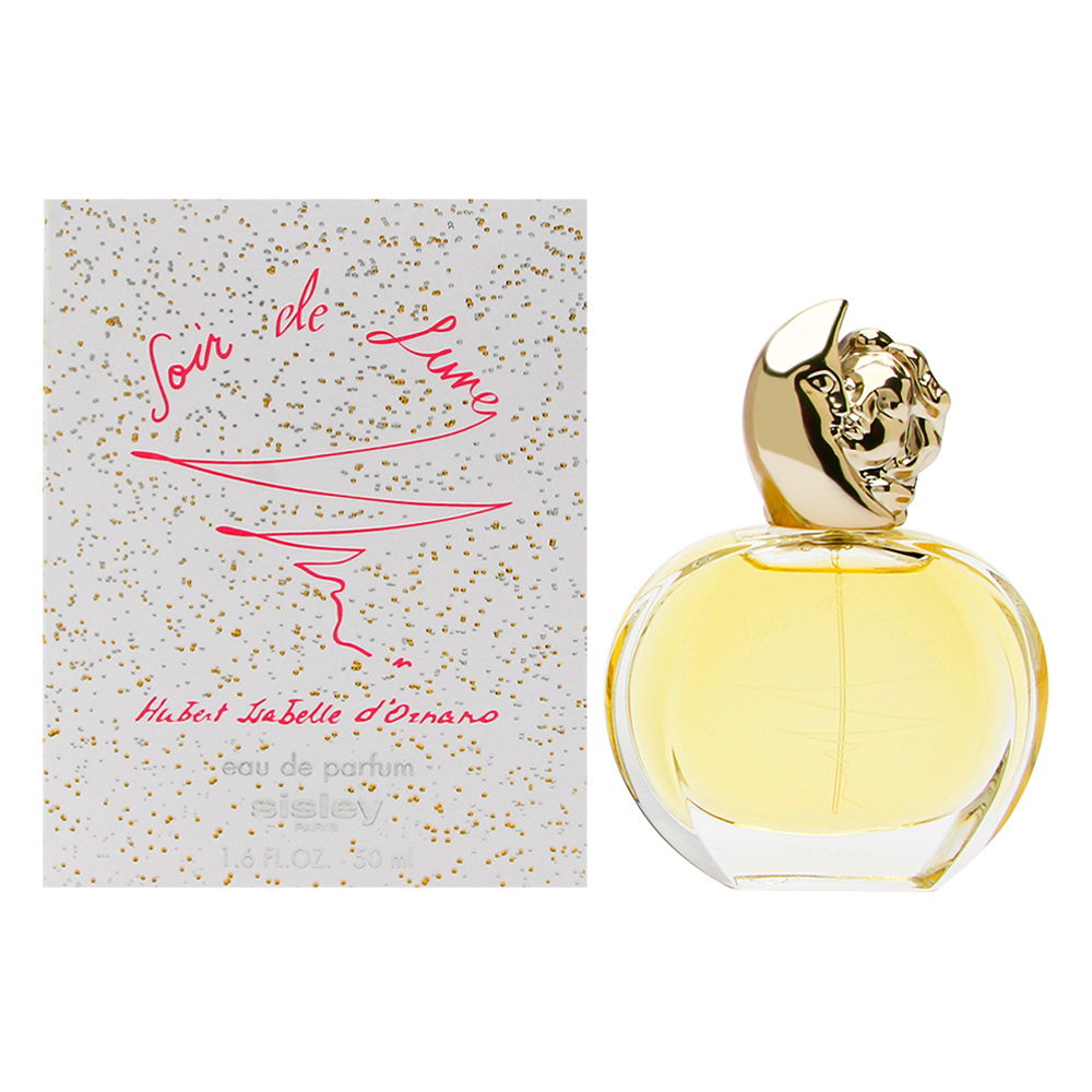 Clear glass bottle with a gold cap shaped like a crescent moon, containing pale yellow perfume, alongside a white box adorned with gold speckles and pink script.