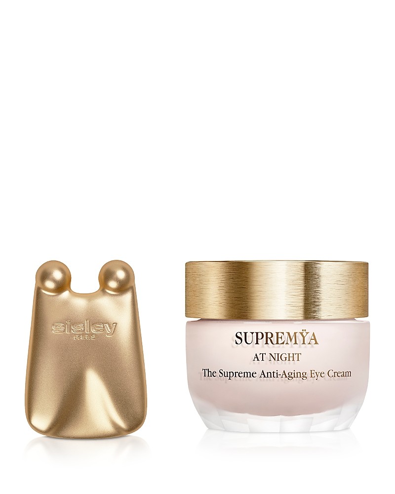 Gold and cream jar of Sisley-Paris Supremya at Night eye cream, featuring a sleek design with a gold lid and a small, gold applicator tool beside it.