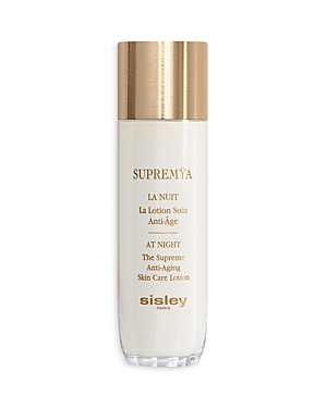 Tall, elegant white bottle with a gold cap, featuring "Supremya at Night" and "Sisley" printed in gold text on the front, designed for anti-aging skin care.