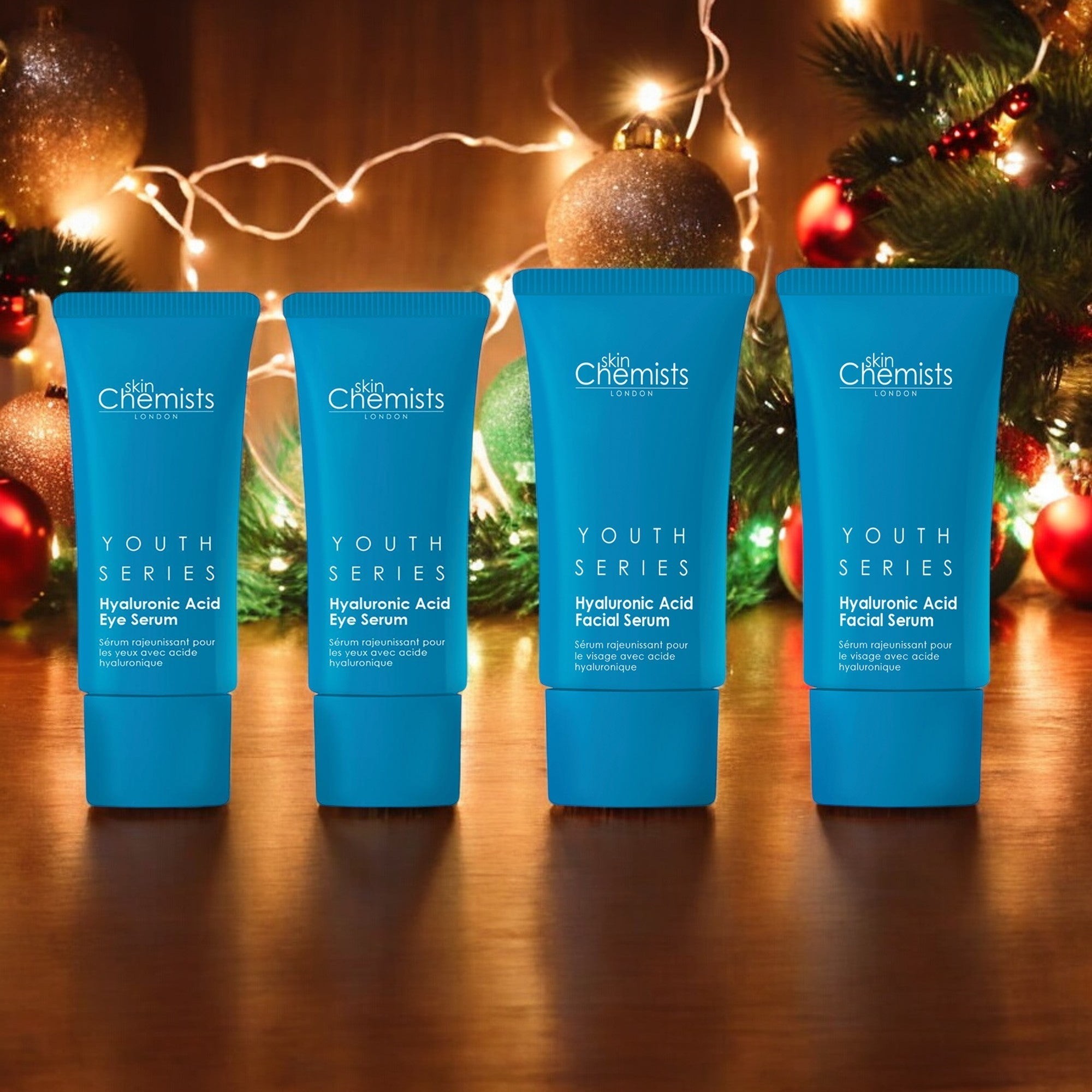 Skinchemists Youth Series Anti-Ageing Hydration Kit featuring two blue tubes labeled "Hyaluronic Acid Eye Serum" and two "Hyaluronic Acid Facial Serum," set against a festive, decorated background.