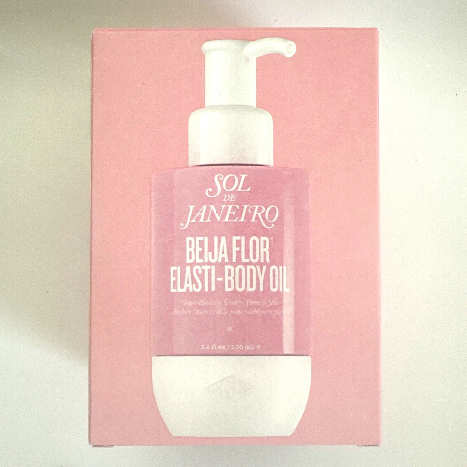 Pink bottle of Sol de Janeiro Beija Flor Elasti-Body Oil with a white pump, displayed on a matching pink box, featuring elegant typography and product details.