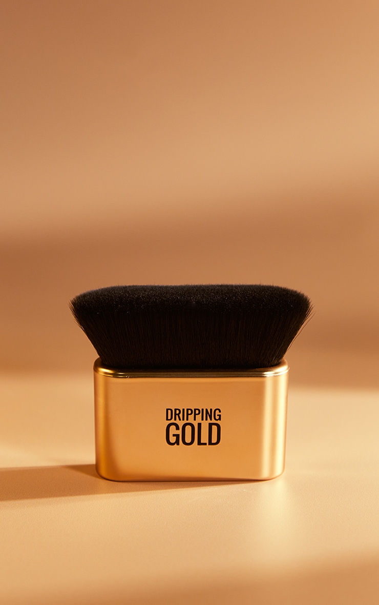 A gold metallic Kabuki brush with a flat, wide black bristle head, labeled "DRIPPING GOLD," designed for contouring makeup application.