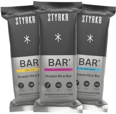 Styrkr Bar+ Recovery Bar 12-pack featuring three flavors: Lemon Drizzle, Raspberry & White Chocolate, and Sea Salted Caramel, each in sleek black packaging with colorful accents.