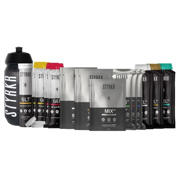 Styrkr Training 7/7 Pack features a black shaker bottle and multiple colorful packets, including yellow, pink, and teal, designed for hydration and energy supplements.