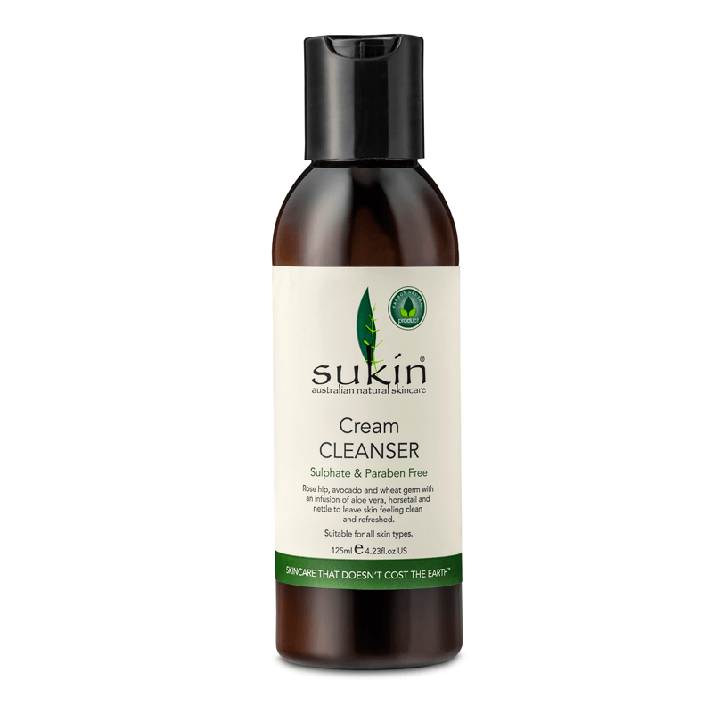 Brown plastic bottle with a black pump cap, labeled "Sukin Cream Cleanser," featuring green accents and text stating it's sulfate and paraben free, suitable for all skin types.